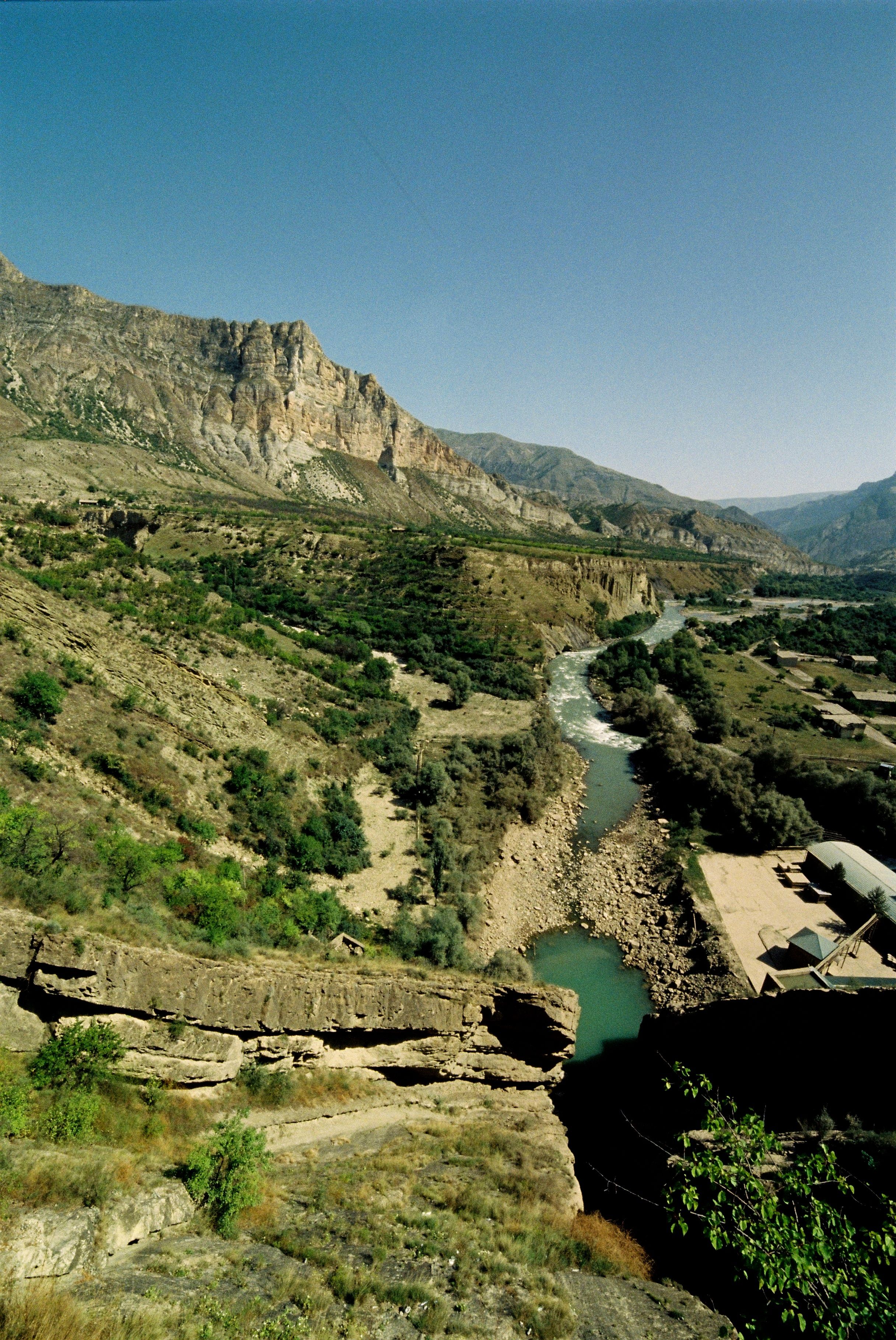 Scenic view of a tranquil river winding through a lush mountain valley under a clear blue sky.