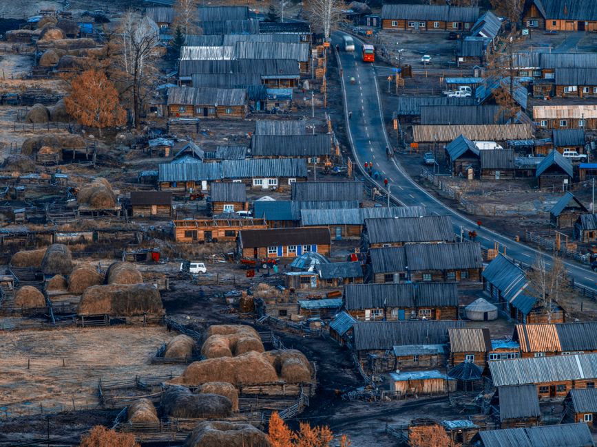 A captivating aerial view of a rural village with hay bales, houses, and a winding road during a fal