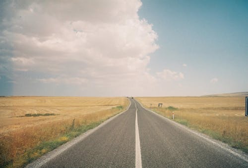 Gray Asphalt Road Between Green Grass Field Under White Clouds and Blue Sky