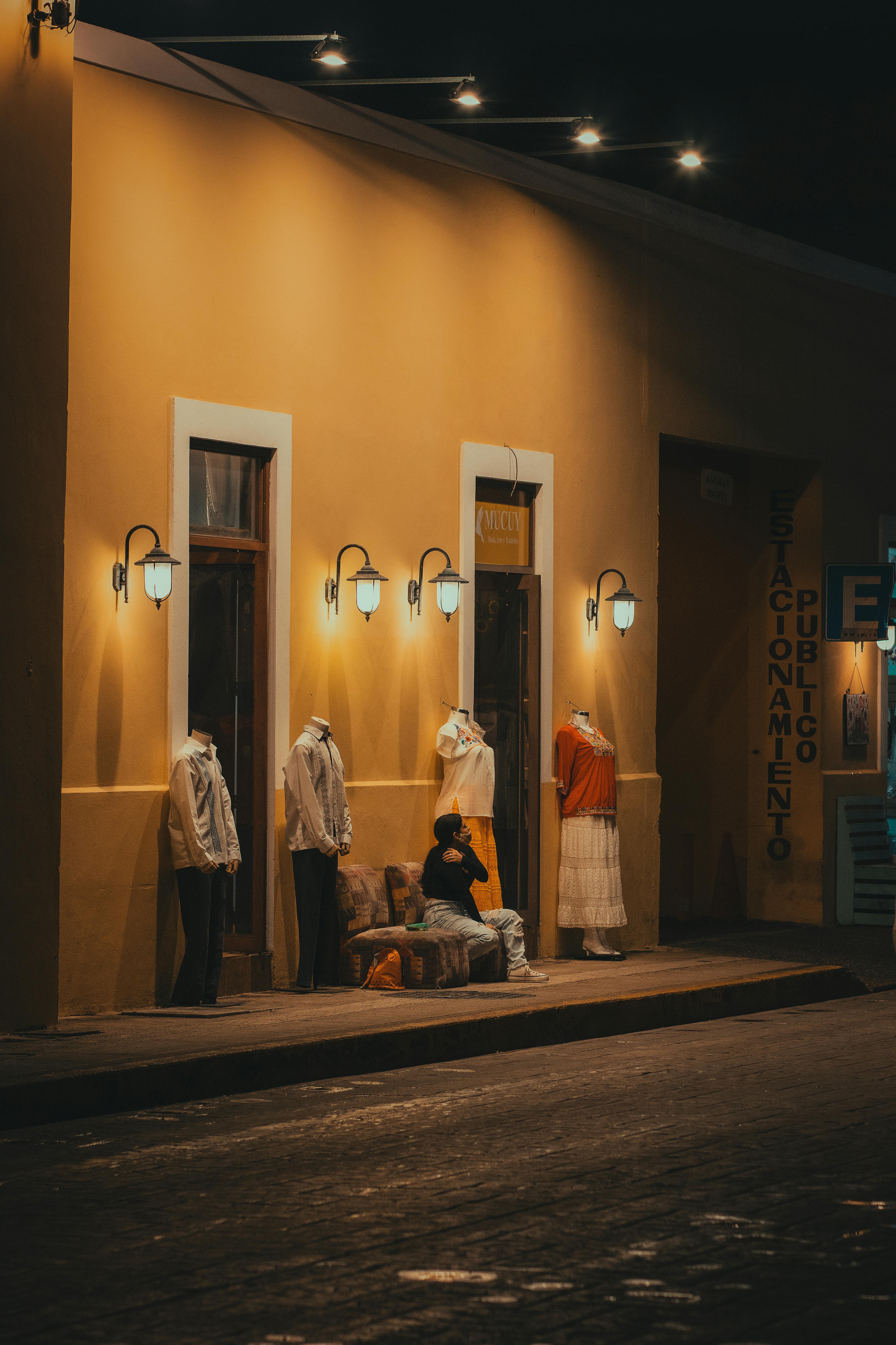 Woman Sitting Between Mannequins Displaying Clothes on the Sidewalk