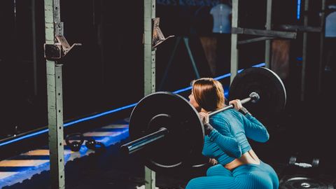 Woman squatting with a barbell in a gym, showcasing strength and fitness focus.
