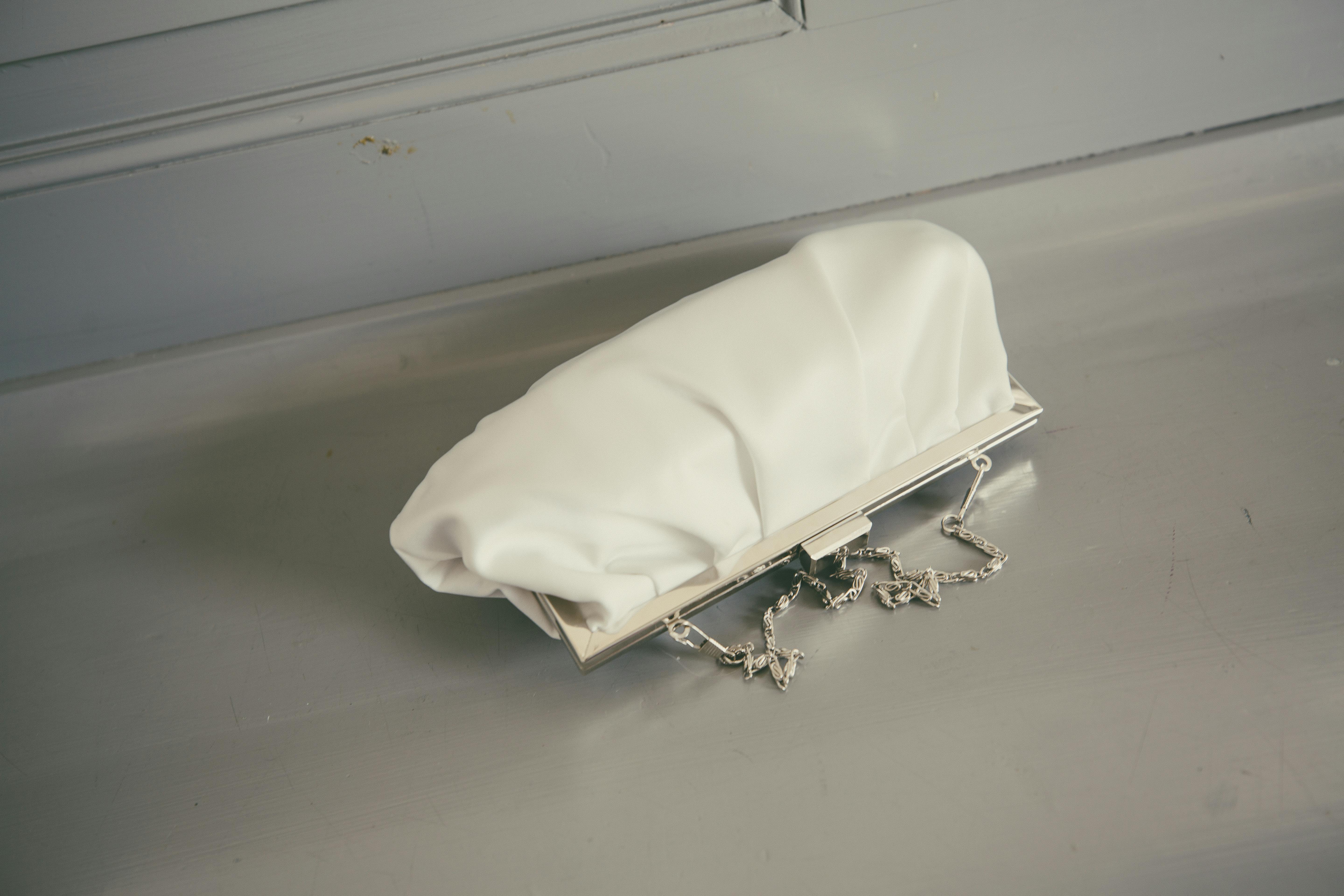 这款白色手拿包设计别致，表面纹理独特，并配有银色链条