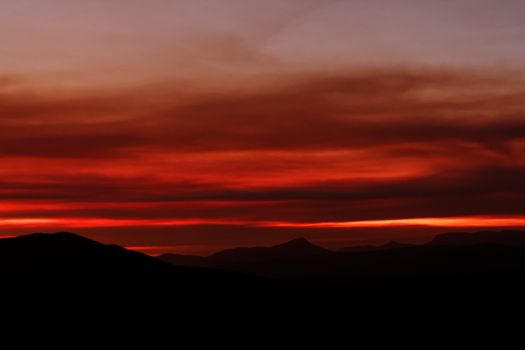 A stunning red sunset casts dramatic light over silhouetted mountains, creating a serene and captivating scene.
