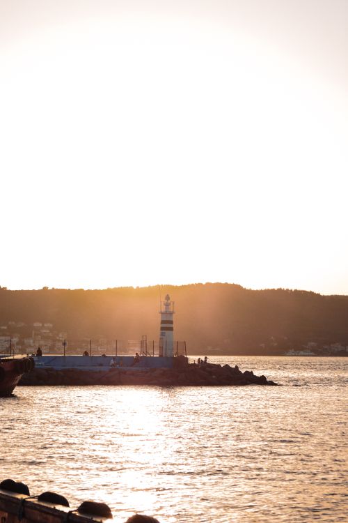 Free Serene sunset view of a lighthouse by the sea, casting silhouettes over the calm waters. Stock Photo