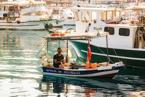 A Man in a Moored Wooden Boat in the Harbor