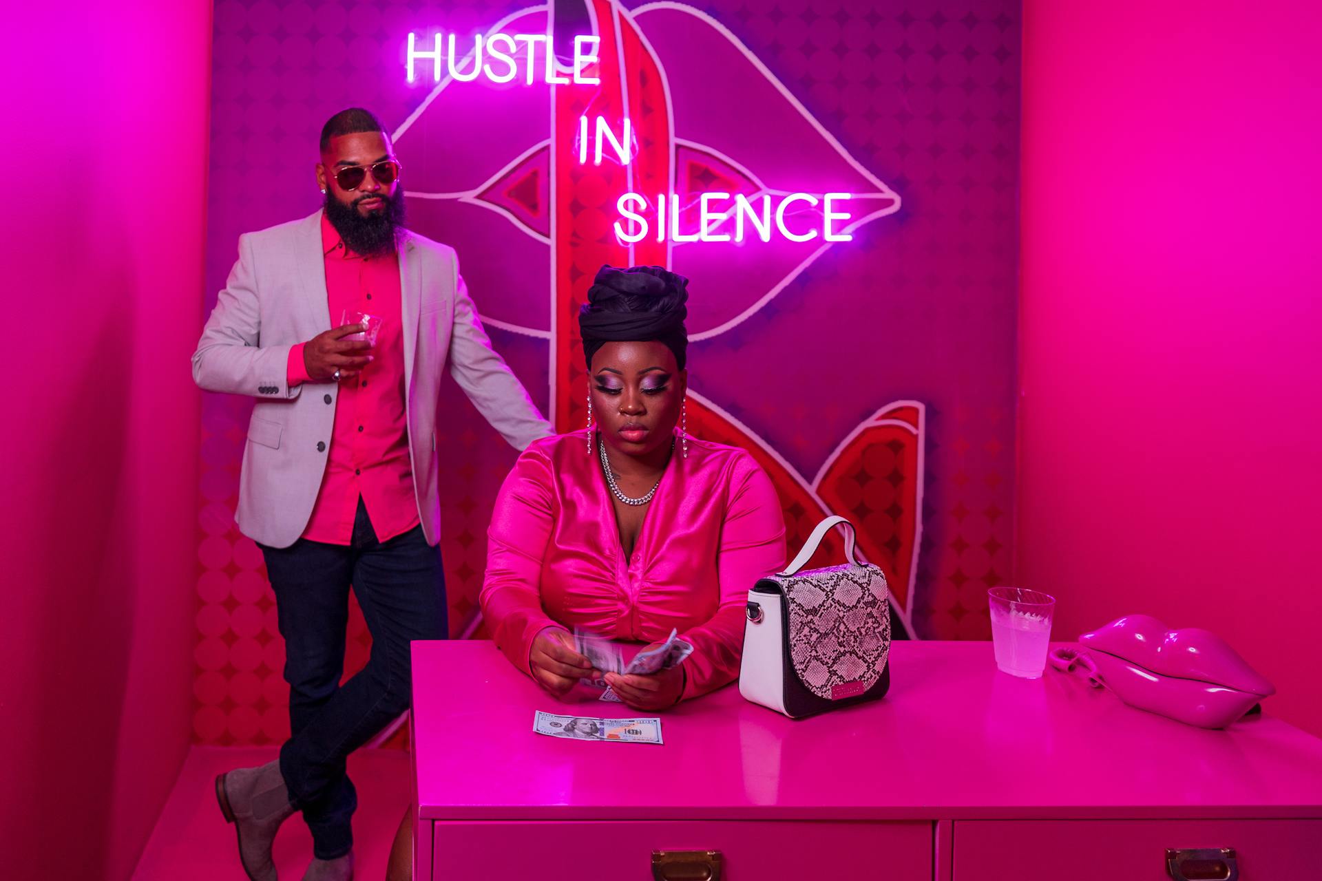 A fashionable couple in a vibrant pink setting counting money, embodying modern hustle and success.