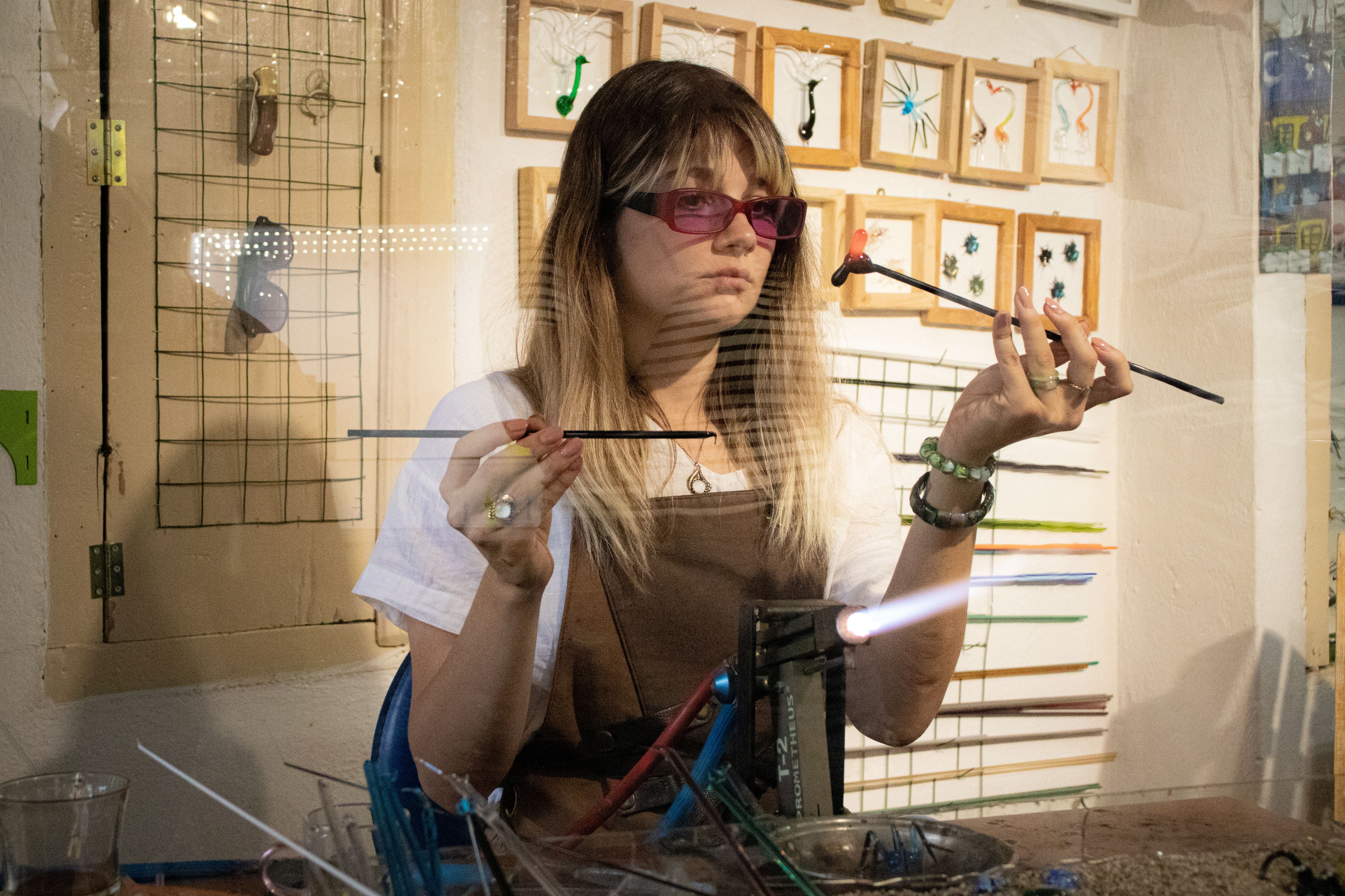 Young woman crafting glass jewelry using a blowtorch in an artisan workshop.