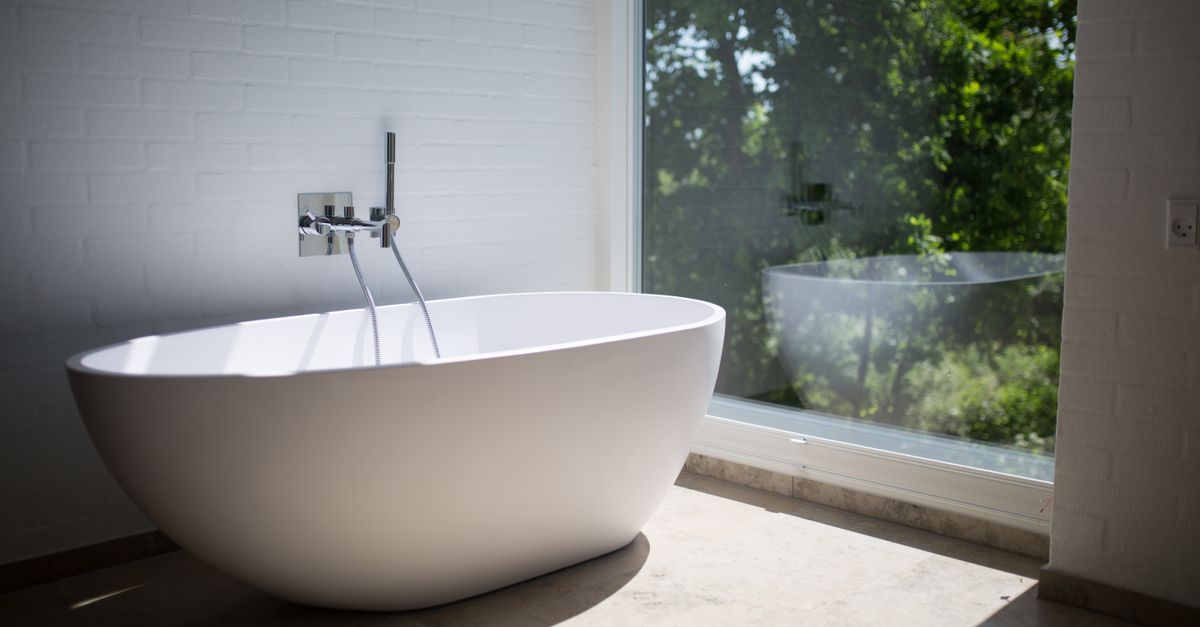 Sleek white bathtub by large window in sunlit minimalist bathroom setting.