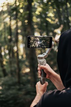 Man using smartphone stabilizer to film scenic forest outdoors.