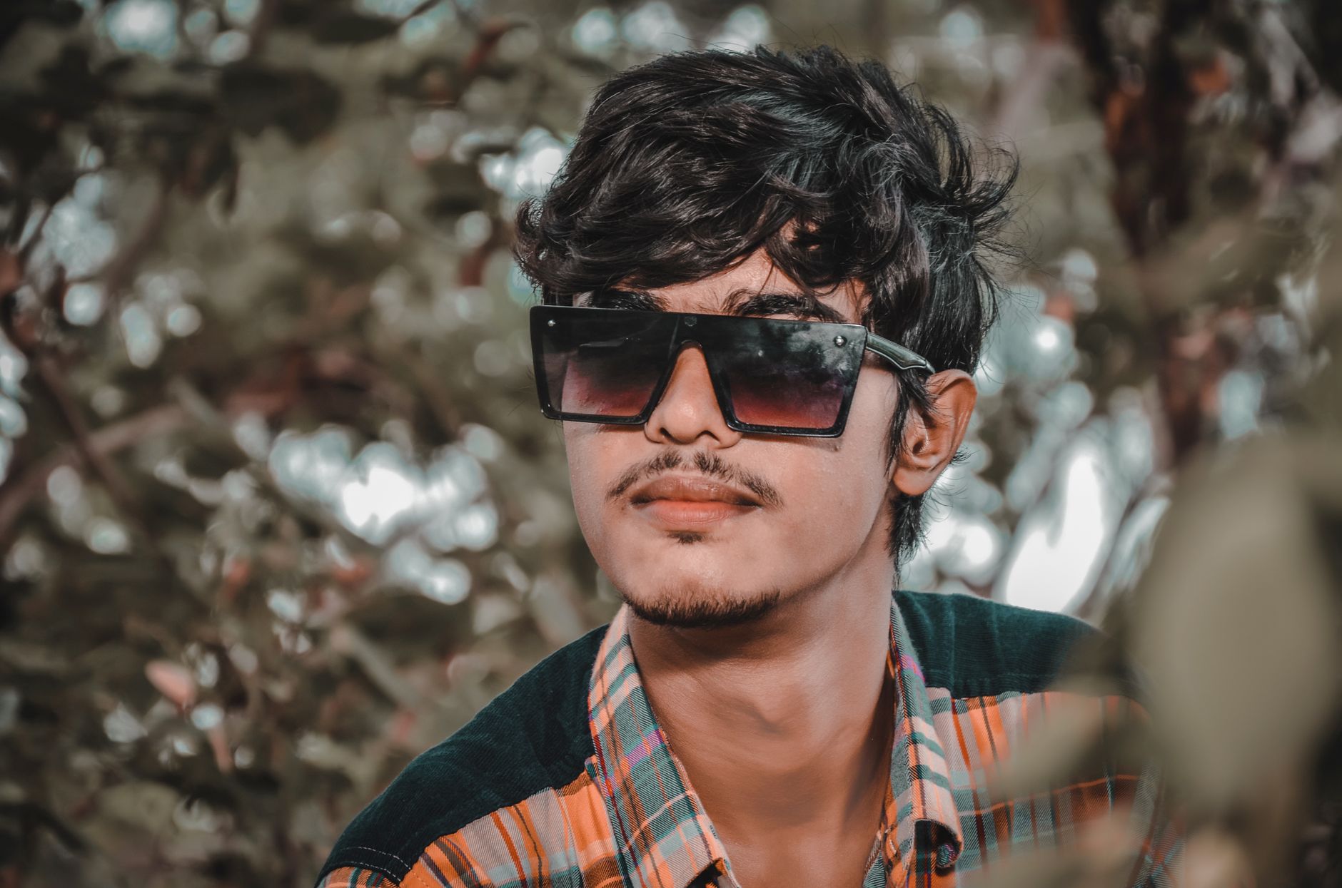 Close-up portrait of a young man with sunglasses and a goatee, amidst an outdoor setting.