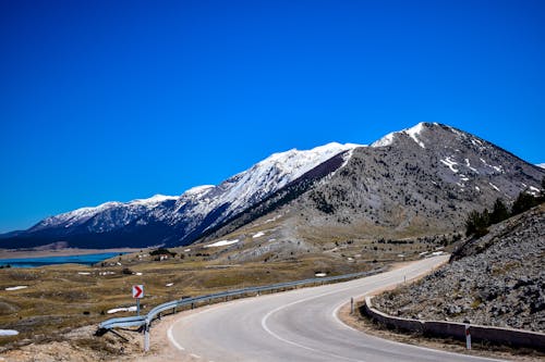 An Empty Road Near the Snow Covered Mountain Under the Blue Sky