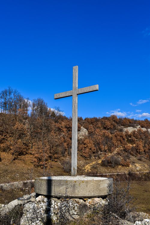 Free A wooden cross on a stone base stands outdoors under a bright blue sky. Stock Photo