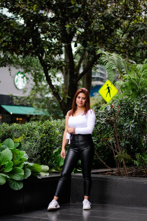 A Woman in Black Leather Pants Standing Near the Green Plants