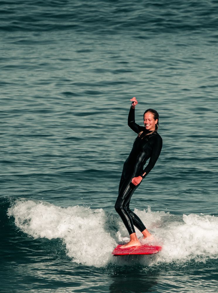 Frau surft auf Longboard im Atlantik mit Neoprenanzug