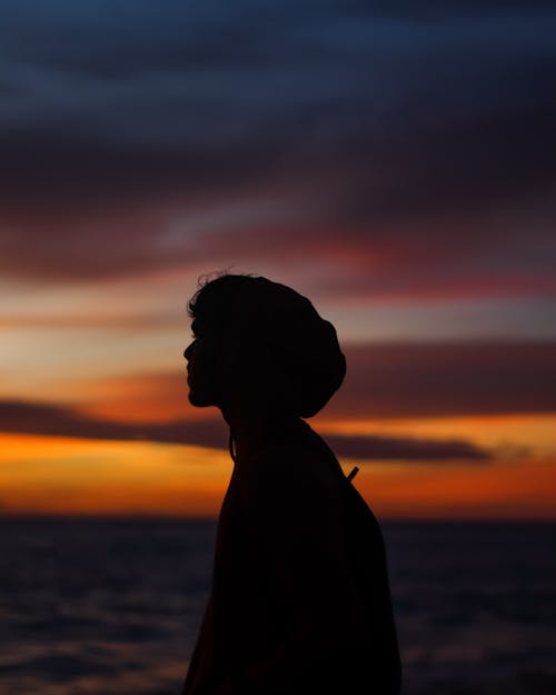 Silhouette of Woman Standing Near Body of Water during Sunset