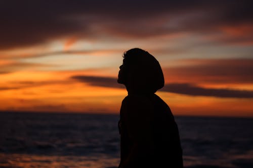 Silhouette of Person in Hoodie on Beach During Sunset
