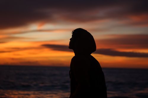 Free Silhouette of a person wearing a hoodie looking at the sunset over the ocean in India. Stock Photo
