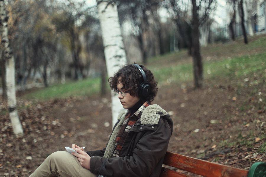 Listener on a park bench in autumn wearing headphones — photo by R&uuml;meysa on Pexels