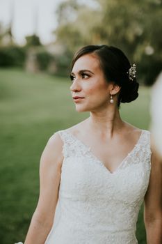Bride in a lace dress looking to the side in an outdoor garden setting