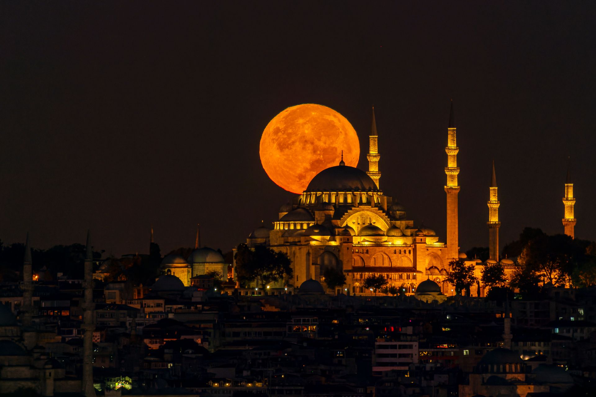 A mosque illuminated at night with the full moon rising above its minarets