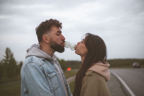 Free Romantic couple blowing a bubblegum bubble together on a scenic road, showcasing love and playfulness. Stock Photo