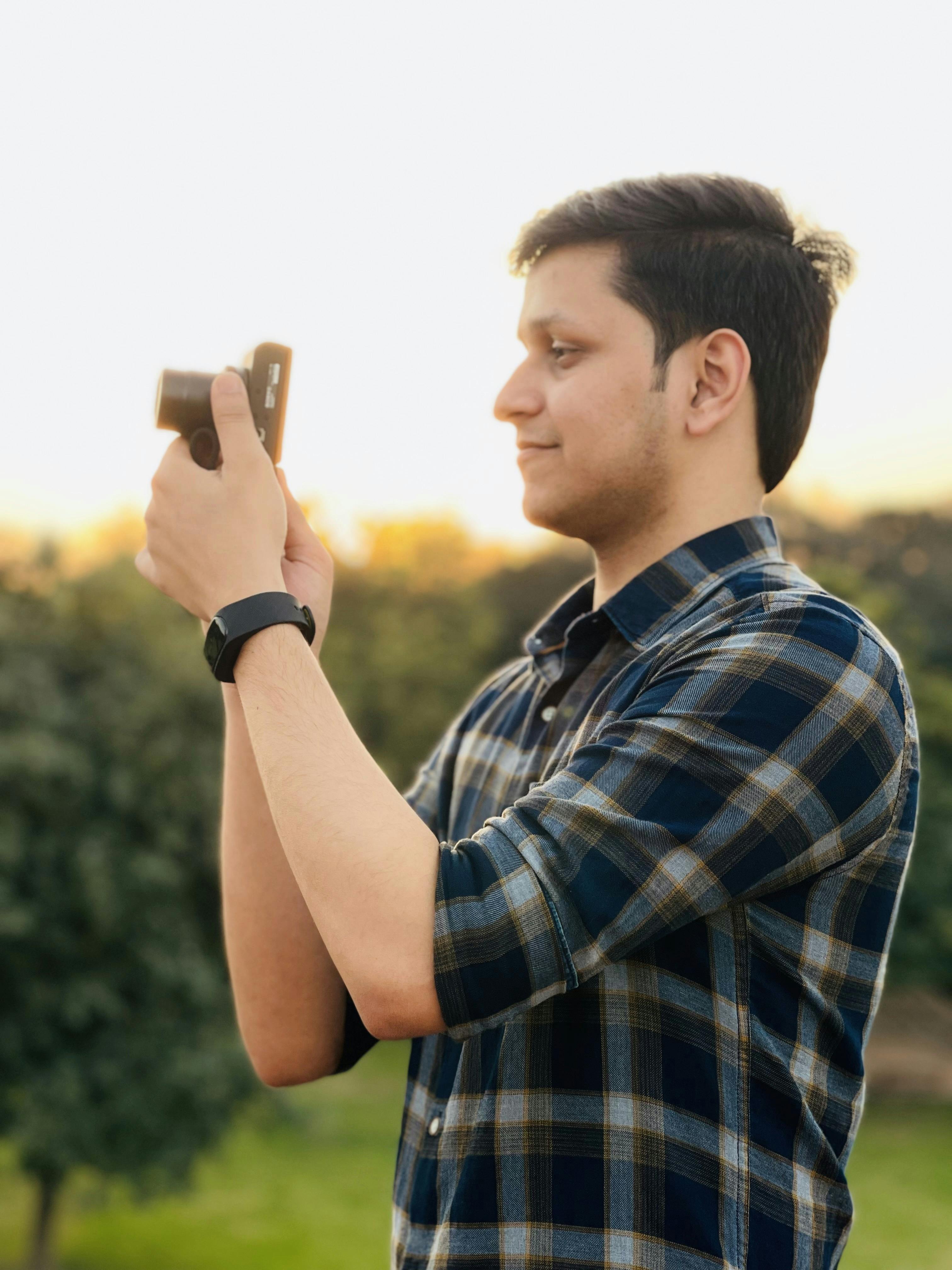 A man in profile view capturing a photo outdoors with a smartphone during the day.