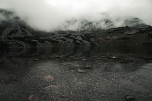 Gray Mountain Covered with Clouds Near Body of Water