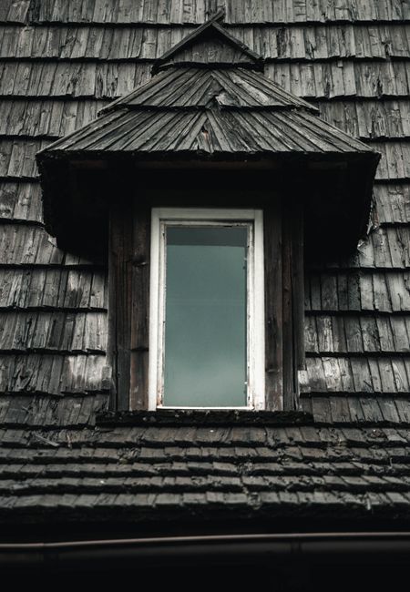 Close-up of an old dormer window with wooden shingles on a traditional roof.