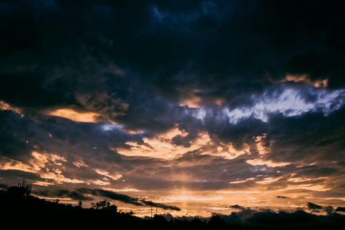 Free Stunning sunset with dramatic clouds and a silhouetted landscape, creating a serene twilight view. Stock Photo