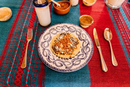 Free Close-up of a Mexican memela served on a vibrant woven tablecloth with silverware in Oaxaca. Stock Photo