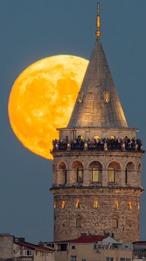 Free Galata Tower illuminated by full moon in Istanbul's night skyline. Iconic historical landmark. Stock Photo