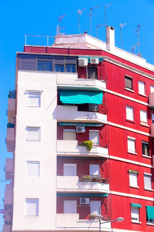 Free Vertical view of a modern residential building facade in Valencia, featuring red exterior and balconies. Stock Photo