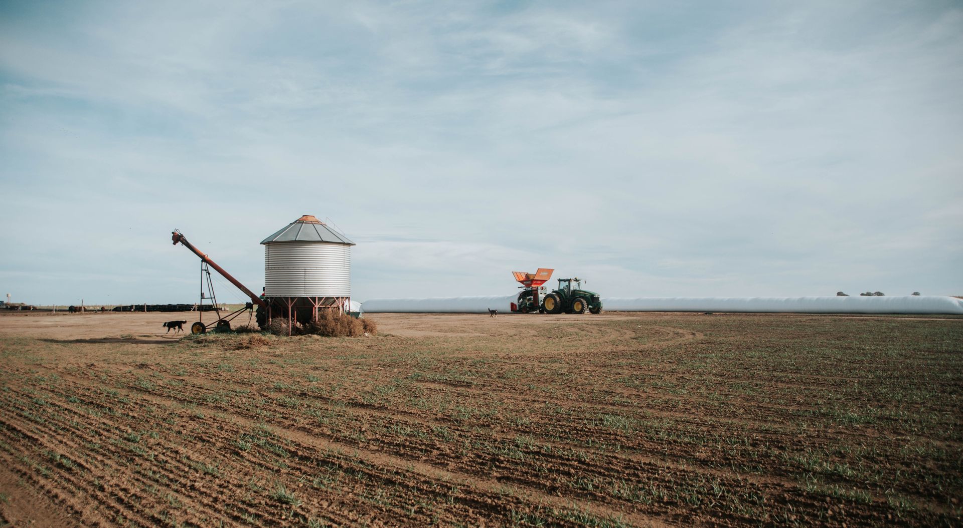 Expansive rural landscape featuring a tractor and grain silo under a vast blue sky.