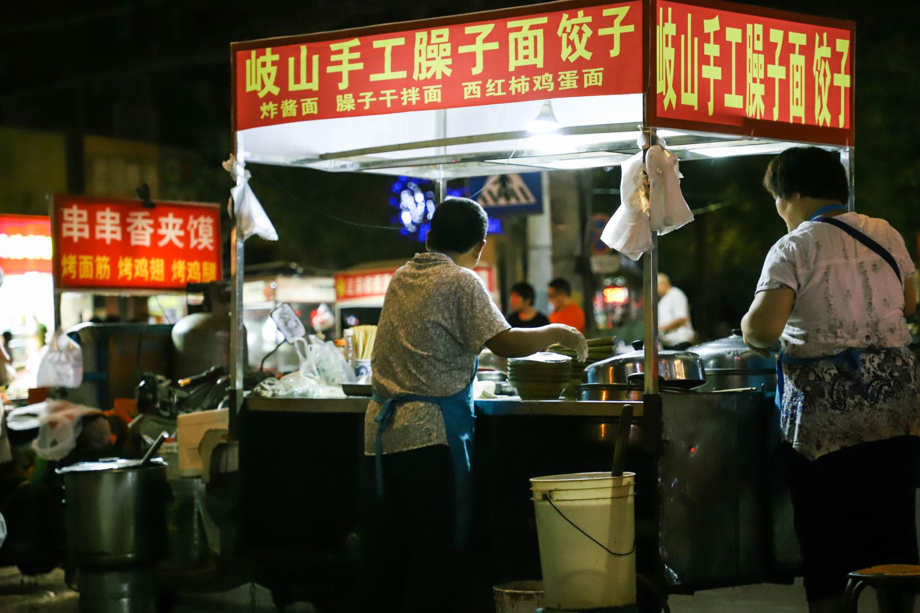 Street food vendors preparing dishes at a bustling night market.