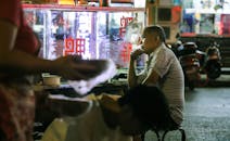 夜市上，一名男子若有所思地坐在小吃摊前