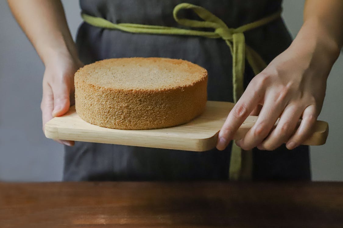 Free Person Holding Chopping Board With Sponge Cake Stock Photo