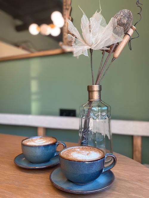 Free Two blue cups of coffee with latte art on a wooden table indoors, next to a glass vase. Stock Photo