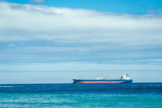 A large cargo ship navigates a calm blue ocean under a partially cloudy sky.