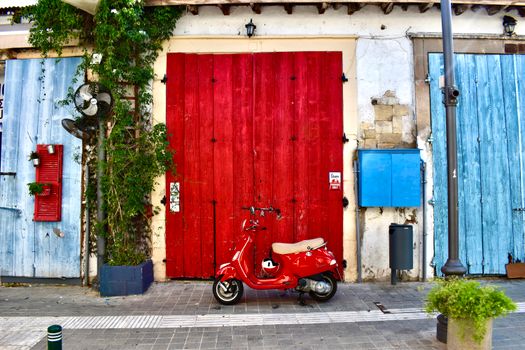 Colorful street scene in Larnaca, Cyprus, with a red scooter and wooden doors.