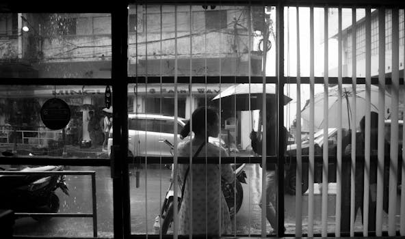 A black and white street view captured through a window on a rainy day.
