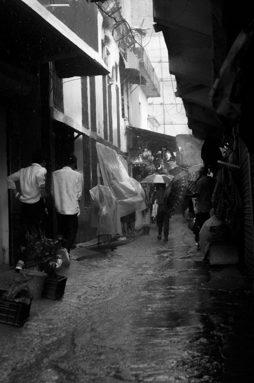 Free Monochrome image capturing people walking through a narrow rainy alley. Stock Photo