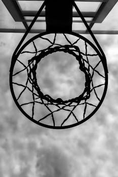 Artistic low-angle black and white shot of a basketball hoop against the sky.