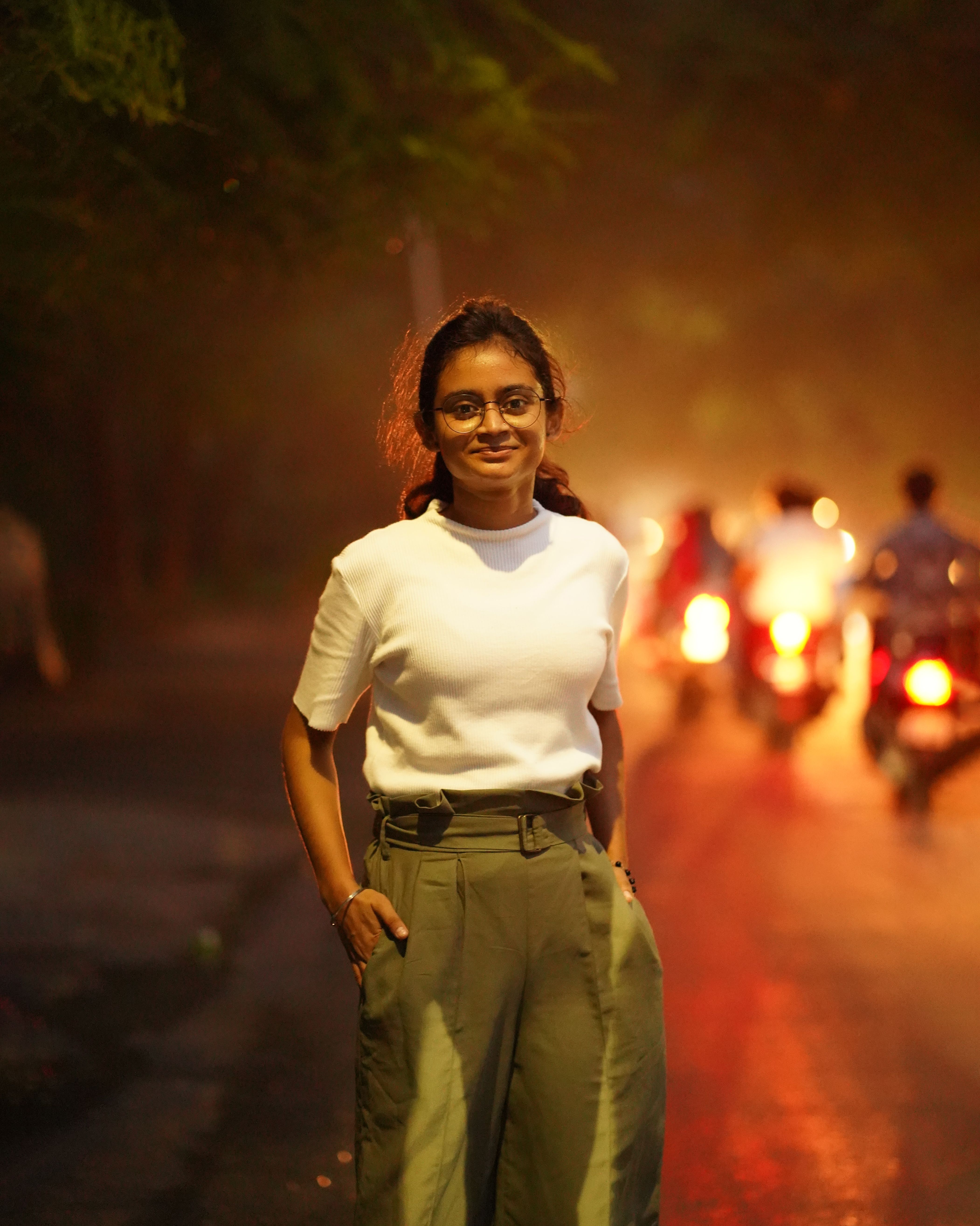 A smiling woman stands confidently on a dimly lit street with motorcycles in the background.