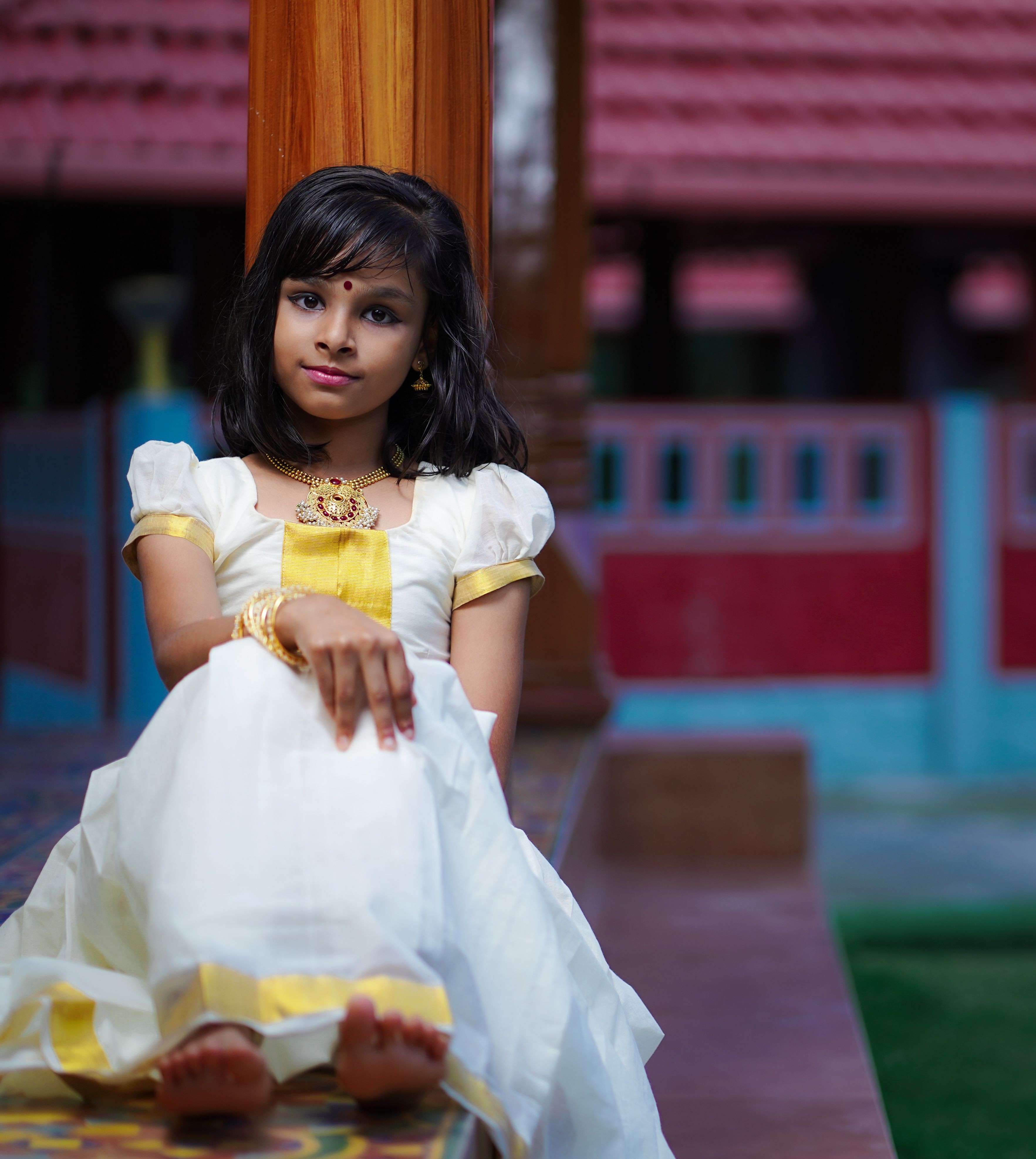 Young Indian girl in a traditional dress, sitting gracefully outdoors.