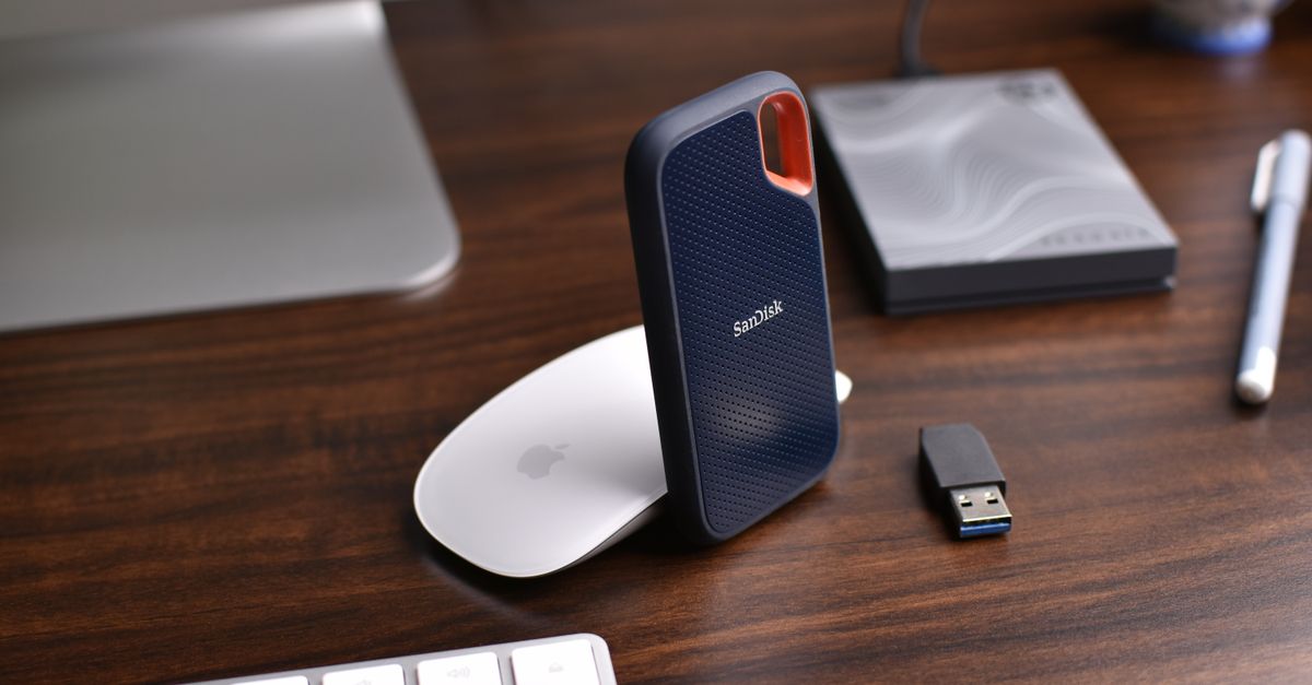 Close-up of a modern desk setup with a SanDisk external hard drive and electronics on a wooden surface.