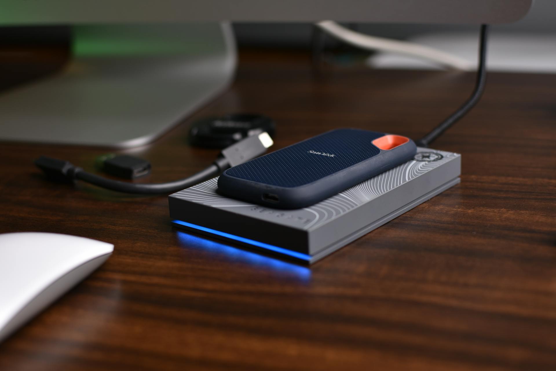 A close-up view of a portable USB SSD placed on a wooden desk with connected cables.