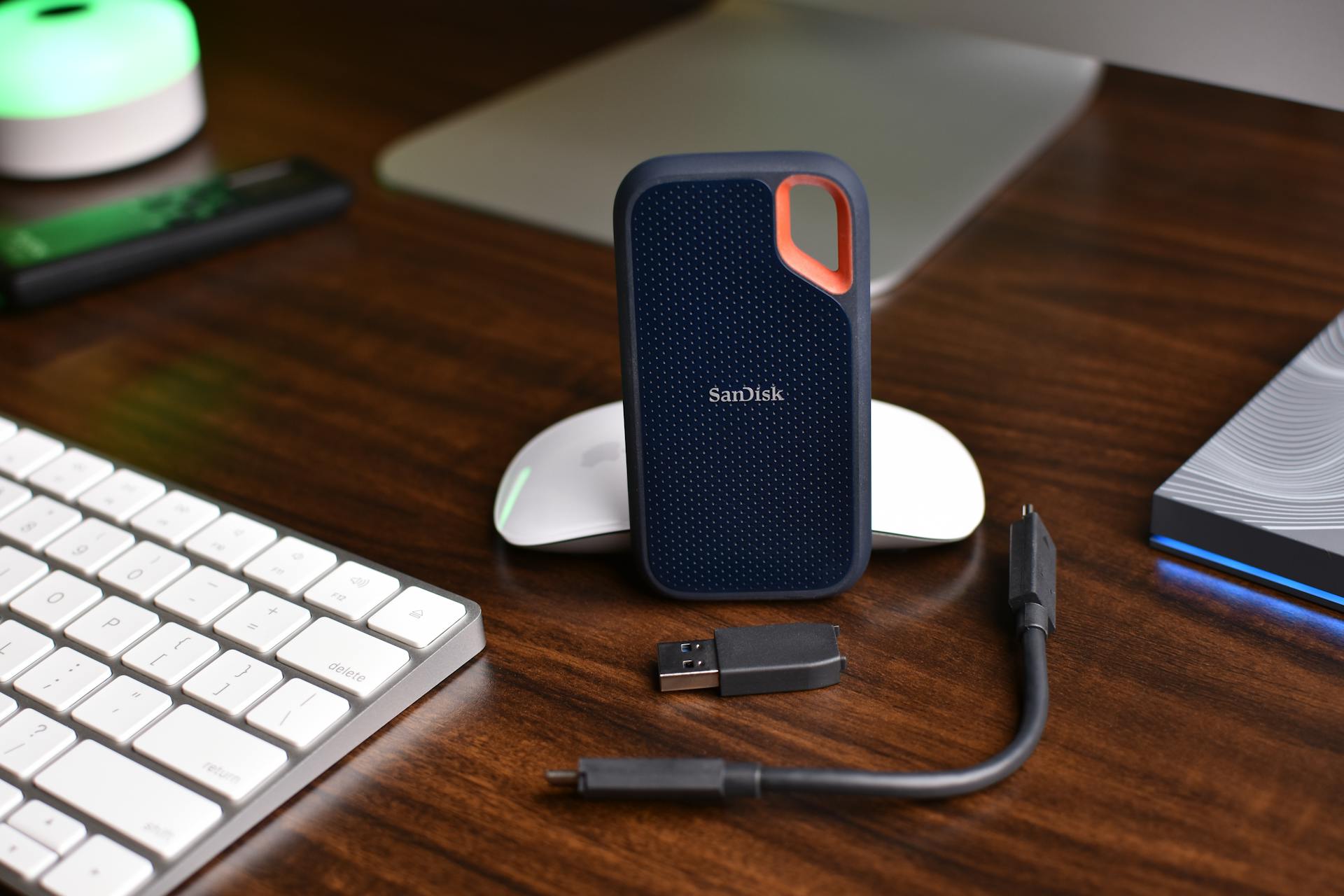 SanDisk portable SSD with USB cable and computer accessories on a wooden desk.