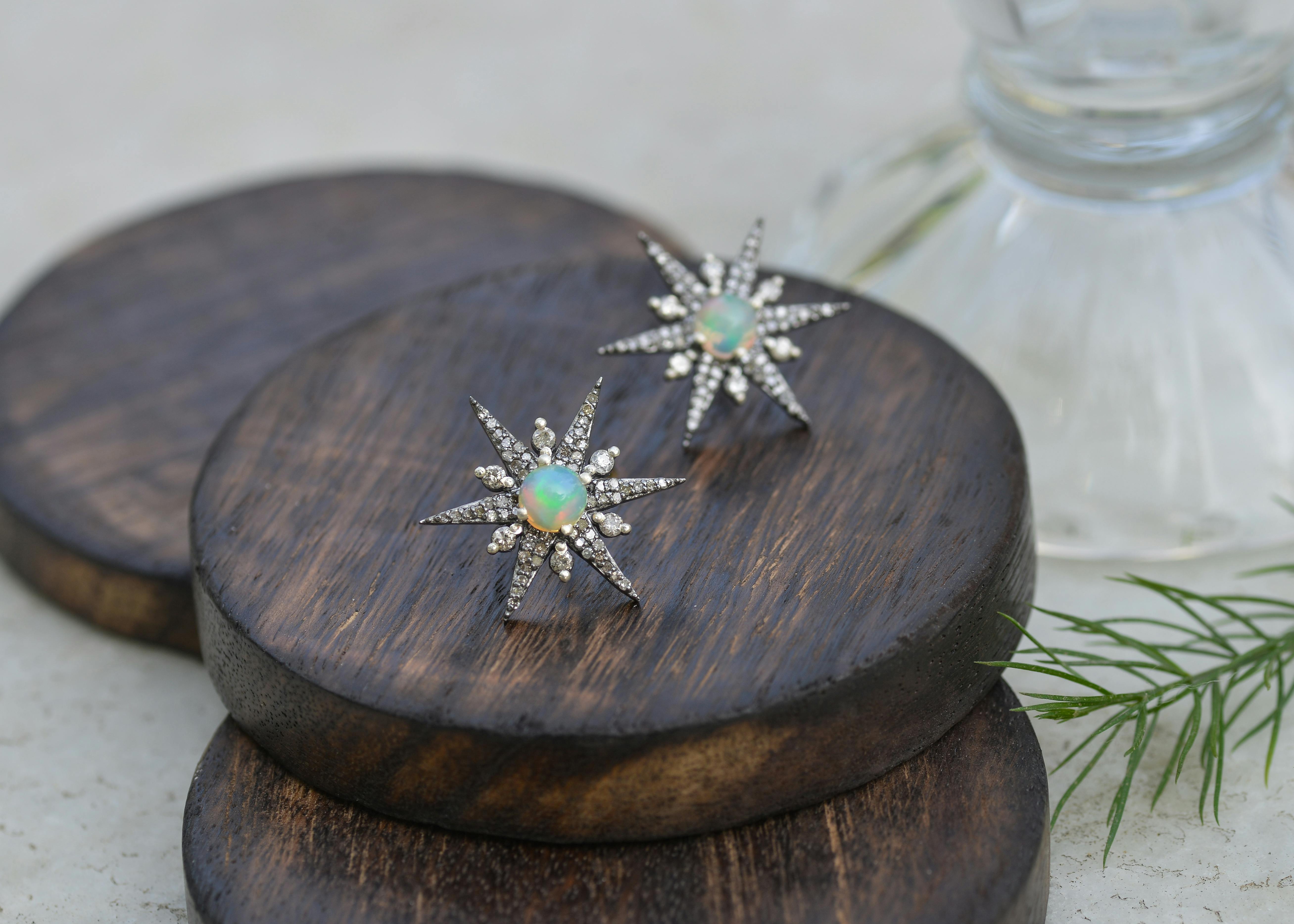 Star-shaped opal and silver earrings displayed on wooden surface, close-up fashion jewelry photography