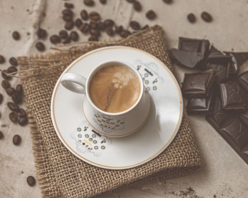 Free Top view of a cappuccino cup with latte art on a saucer, surrounded by chocolate and coffee beans. Stock Photo