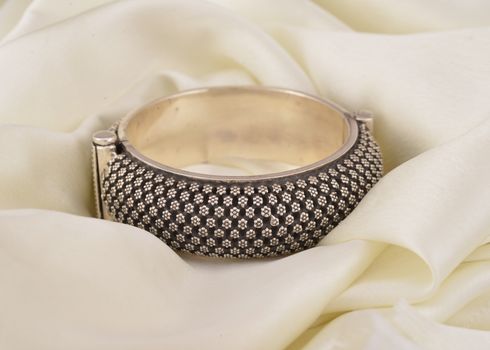 Close-up of a detailed silver bracelet elegantly displayed on a soft white textile.